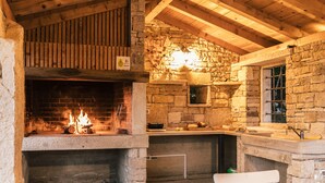 Une cheminée en pierre rustique avec un feu de bois, un plafond en bois et un mur en pierre avec une fenêtre.