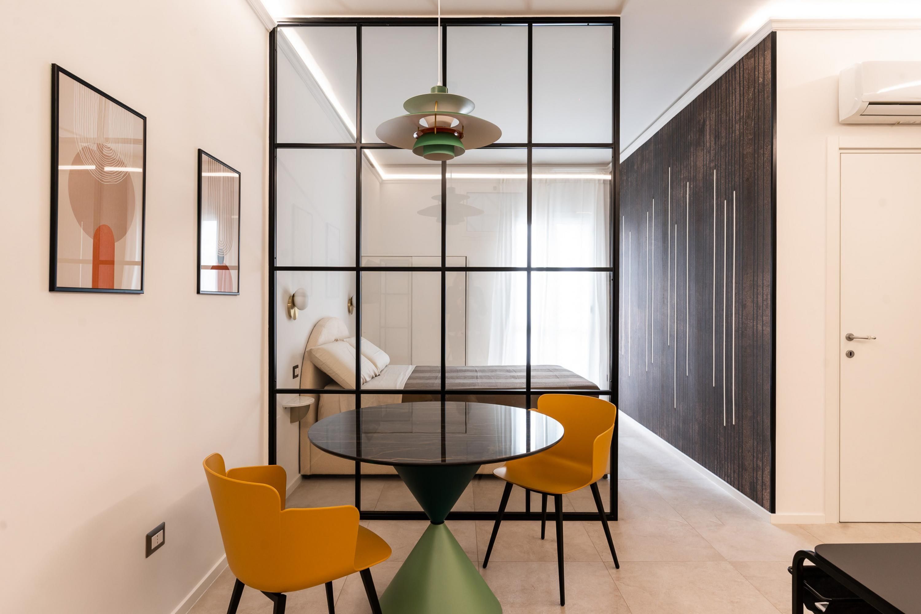 A modern dining area with a round table, yellow chairs, and a green pendant light.