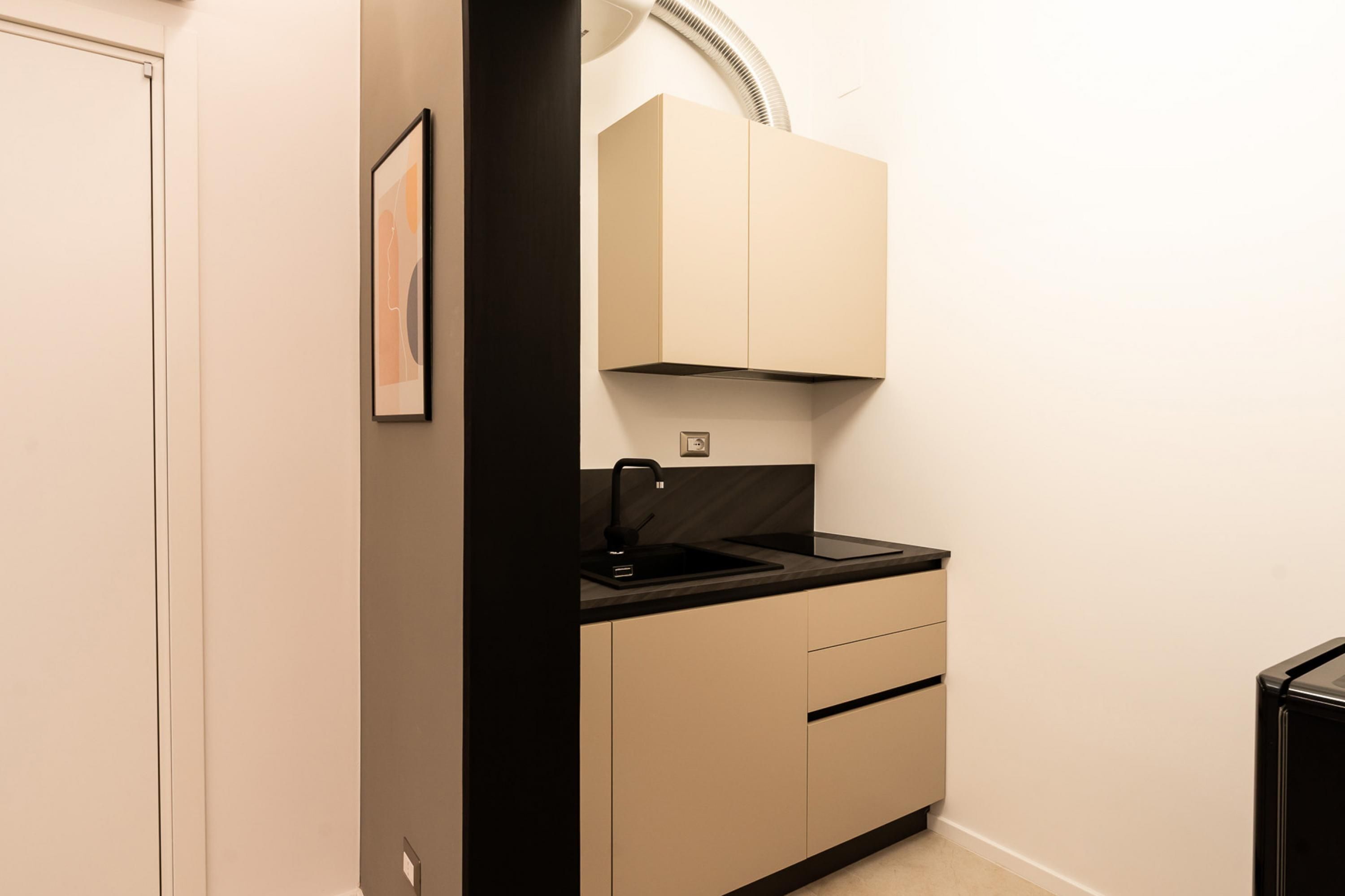 Une cuisine compacte avec un évier noir, des armoires de couleur beige et un petit plan de travail.
