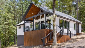 A modern cabin with a wooden deck, large windows, and a staircase leading to an upper level. - Alpine Amorè in Hochatown/Broken Bow, OK (Broken Bow)