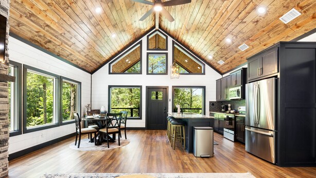 A spacious kitchen with a large island, dark cabinetry, and a stainless steel refrigerator. - Alpine Amorè in Hochatown/Broken Bow, OK (Broken Bow)