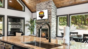 A modern kitchen with a granite countertop, a stone fireplace, and a view of the outdoors. - Alpine Amorè in Hochatown/Broken Bow, OK (Broken Bow)