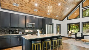 A modern kitchen with dark cabinets, stainless steel appliances, and a large island with stools. - Alpine Amorè in Hochatown/Broken Bow, OK (Broken Bow)