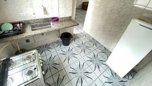 A kitchen with a gas stove, a sink, and a refrigerator. - Suites - Foot on the sand Canto do Forte Beach (Praia Grande)