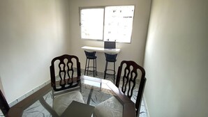 A small dining area with a glass table, two wooden chairs, and a laptop on a white desk. - Suites - Foot on the sand Canto do Forte Beach (Praia Grande)