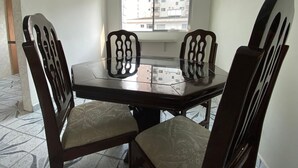 Un comedor con una mesa redonda y cuatro sillas, una ventana con vistas a edificios, y piso de baldosas.