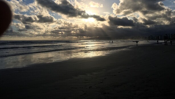 Una playa con el sol poniéndose tras las nubes, creando el perfil silueteado de la costa.
