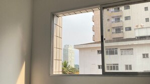 Habitación con ventana que da a un edificio. Se ve una silla en primer plano y un estante pequeño debajo de la ventana.