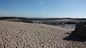 Une plage de sable avec des affleurements rocheux et une vue dégagée sur l’océan.