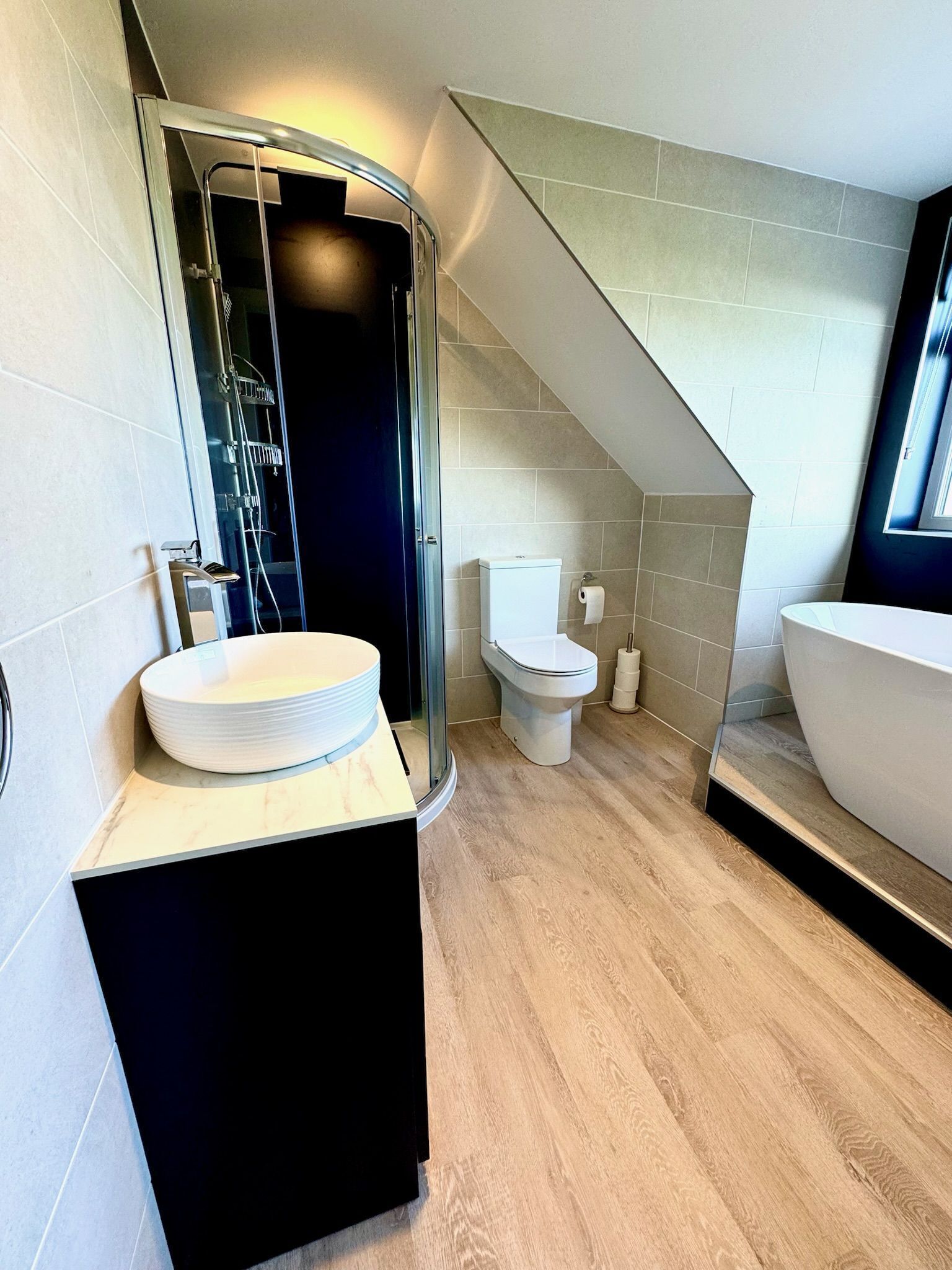 A modern bathroom with a glass-enclosed shower, a white sink with a black countertop, a toilet, and a large bathtub.