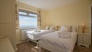 A bedroom with two beds, a window with curtains, a bedside table with a lamp, and a radiator.