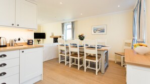 A modern kitchen with white cabinets, a wooden countertop, and a dining area with white chairs and a table.