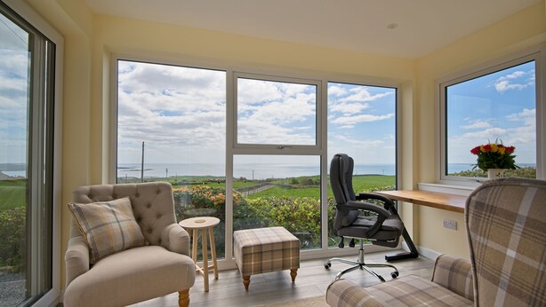 A room with a large window, a chair, a small table, and a desk with a chair.