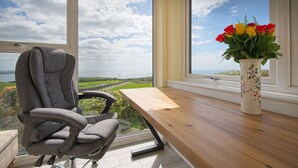 A modern room with a view of the countryside, a grey office chair, and a wooden table with a vase of flowers.