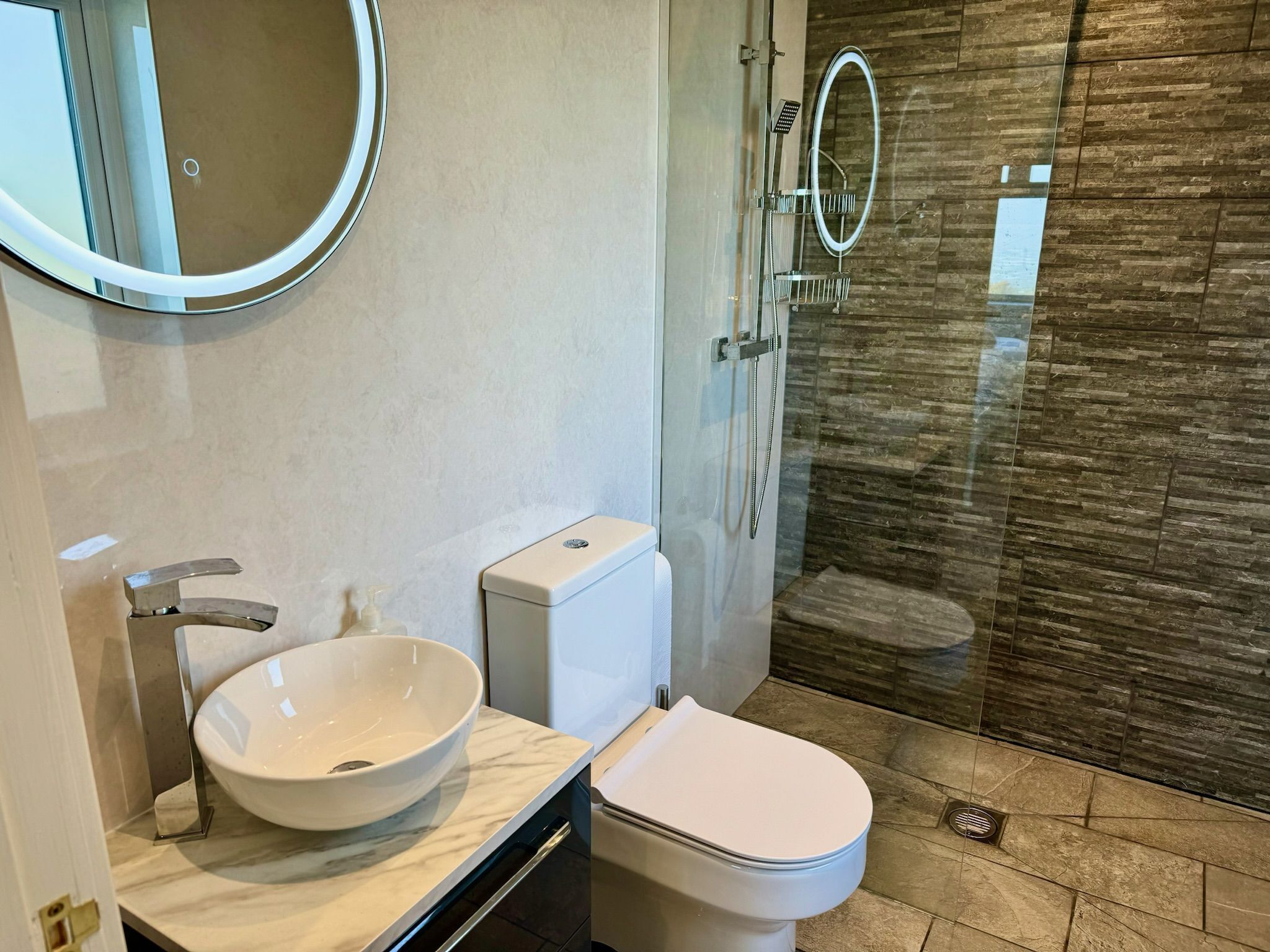 Un baño moderno con lavamanos blanco, inodoro y ducha con mampara de vidrio.