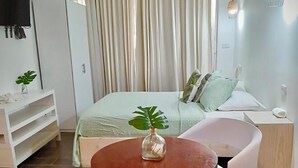 A modern bedroom with a bed, a bedside table, a small round table with chairs, and a TV mounted on the wall. - Hostal Magallanes Bayahibe (San Rafael del Yuma)
