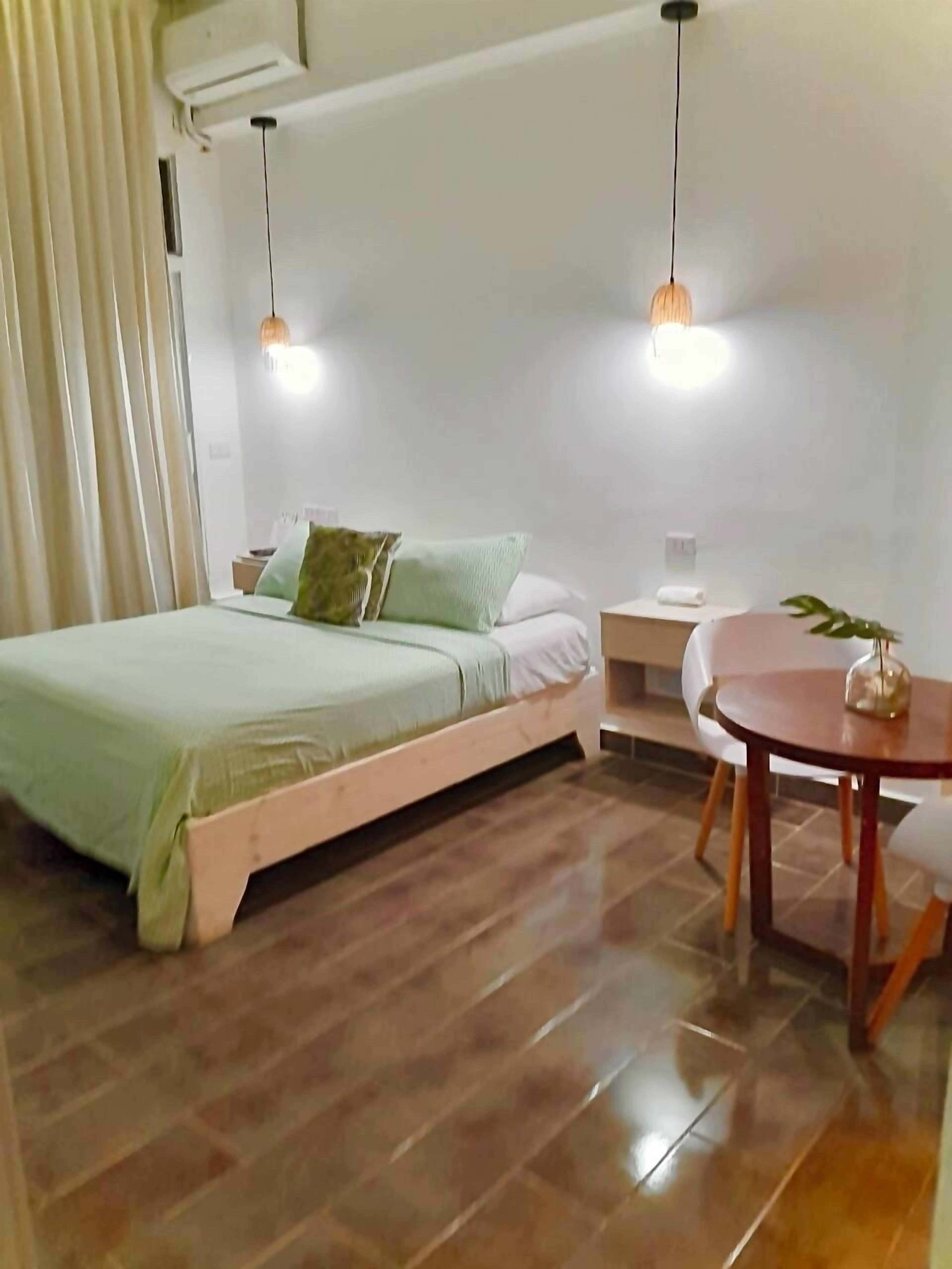 A bedroom with a bed, bedside table, and a small round table with a plant.