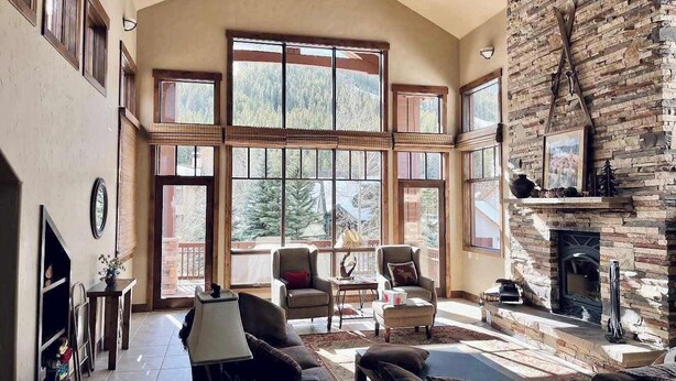 A spacious living room with a fireplace, large windows, and a high ceiling. - Ski-In/Out 5 BR House at Copper Mtn (Frisco)
