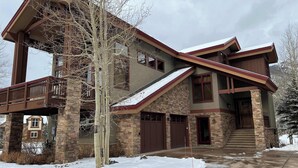 A multi-story house with a stone facade, a wooden deck, and a snow-covered driveway. - Ski-In/Out 5 BR House at Copper Mtn (Frisco)