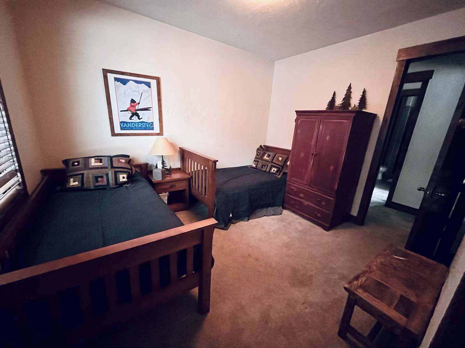 A bedroom with two beds, a wooden wardrobe, a framed picture on the wall, and a small table.