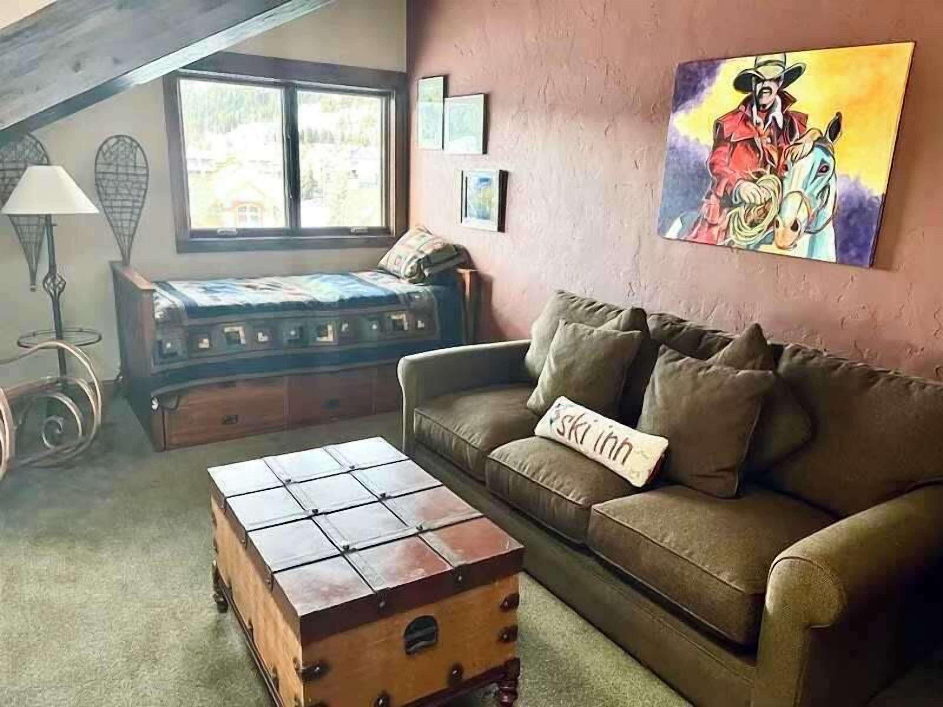 A cozy living room with a sofa, a wooden chest, a lamp, and a painting on the wall.