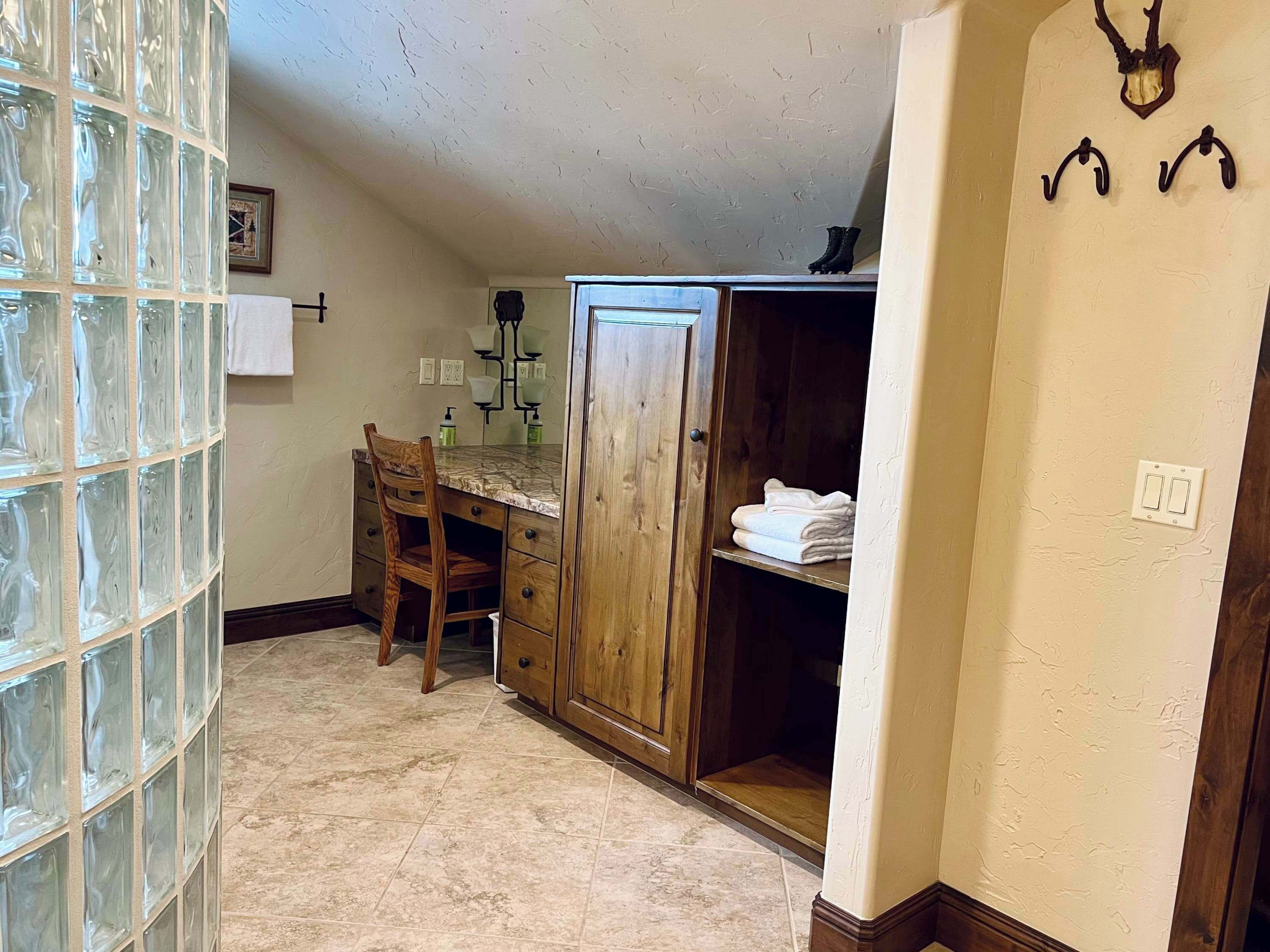 Une salle de bain avec une cloison en verre, une chaise en bois, une commode avec un miroir, un porte-serviettes et un meuble contenant des serviettes pliées.