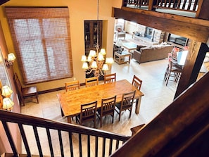 A dining area with a wooden table and chairs, a chandelier, and a view of the living room below. - Ski-In/Out 5 BR House at Copper Mtn (Frisco)