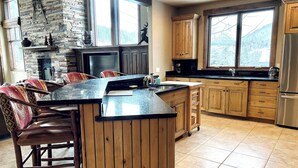 A kitchen with a stone fireplace, wooden cabinets, and a large island with bar stools. - Ski-In/Out 5 BR House at Copper Mtn (Frisco)