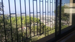 Varanda com grade de metal, vista para a paisagem urbana e vegetação.