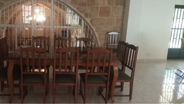 A dining area with a stone wall, a large window with bars, and a chandelier. - Beit Nemer Chemlan Arch house private garden sunset valley view 24/7 Electricity (Chemlan)