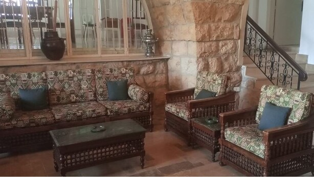 Uma sala de estar com sofás e poltronas estampados, uma mesa de centro e um pilar de pedra.