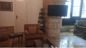 A cozy living room with a stone wall, a television mounted on the wall, and a comfortable seating area with a sofa and armchairs. - Beit Nemer Chemlan Arch house private garden sunset valley view 24/7 Electricity (Chemlan)