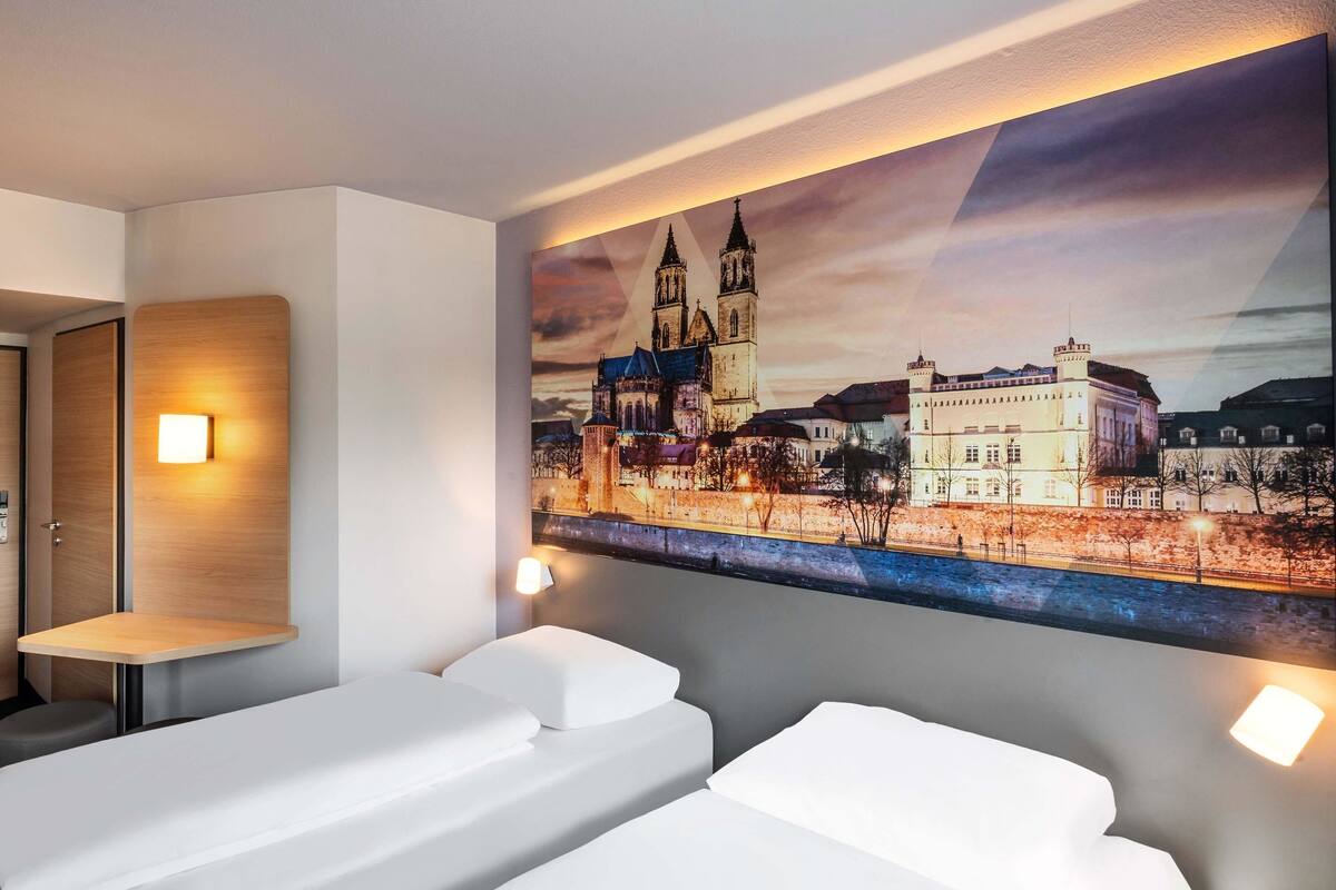 Een hotelkamer met twee bedden, een stadsgezicht op het doek en een klein tafeltje.