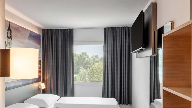 Een hotelkamer met een bed, een televisie, een raam met gordijnen en een lamp.