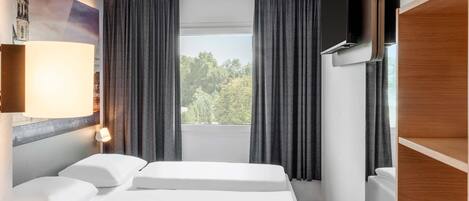 Une chambre d’hôtel avec un lit, une télévision, une fenêtre avec des rideaux et une lampe.