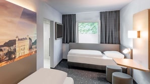 Hotelkamer met een bed, een bureau, een stoel, een klein krukje, een televisie en een schilderij van een kasteel.