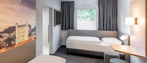 Hotelkamer met een bed, een bureau, een stoel, een klein krukje, een televisie en een schilderij van een kasteel.