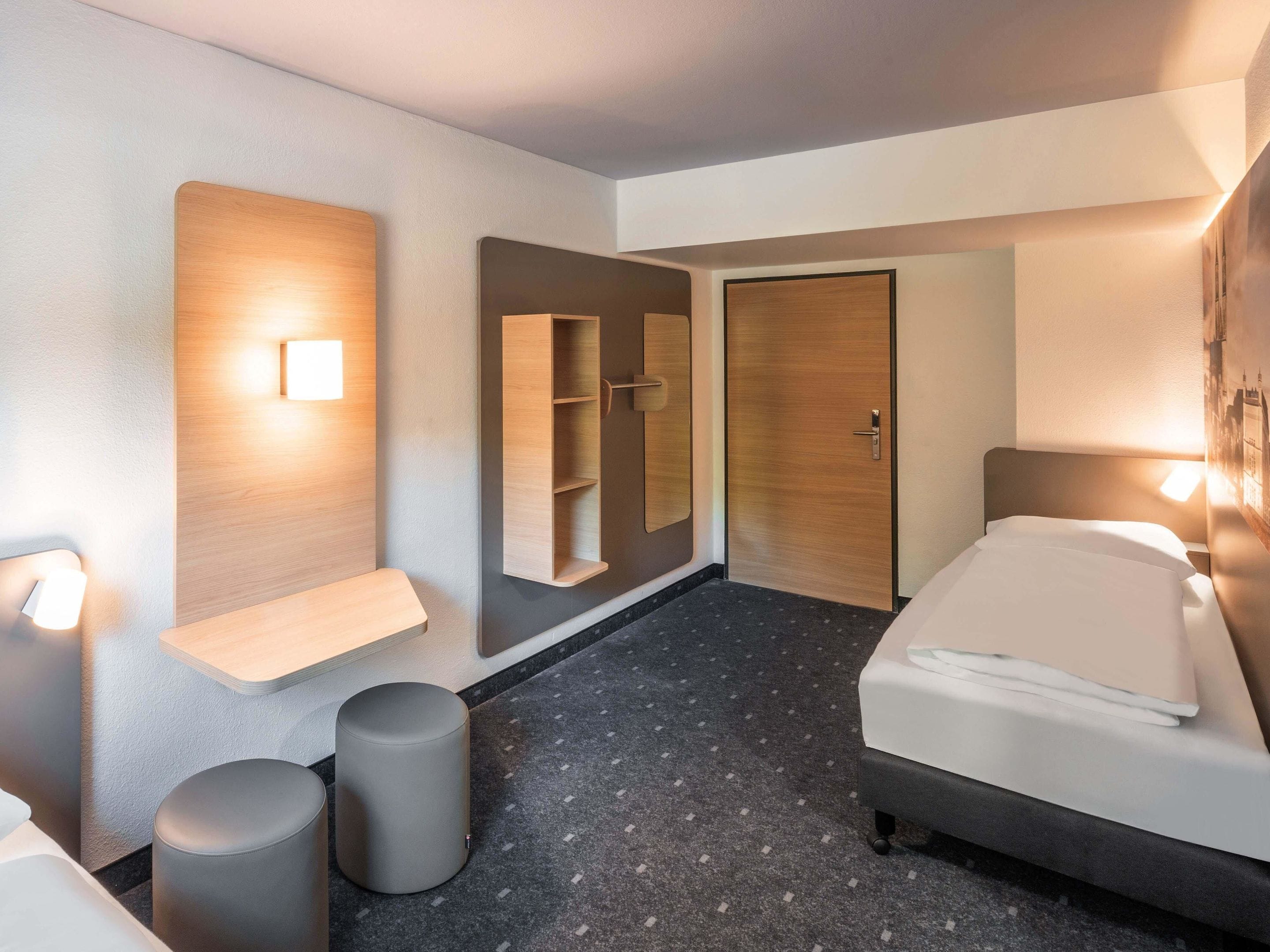 Ein modernes Hotelzimmer mit Bett, Nachttisch, Wandregal, Tür und Mülleimer.