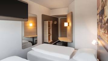 A hotel room with two beds, a mirror, a shelf, and a wall-mounted light.
