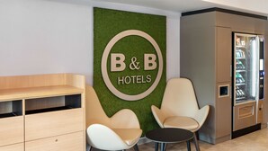 L’espace d’accueil d’un hôtel-restaurant proposant des chambres et le petit-déjeuner, avec deux chaises, un bureau et un distributeur automatique.