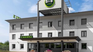Een B&B hotel met een modern ontwerp, voorzien van een opvallend logo op de gevel, meerdere ramen en een overdekt entreegebied.