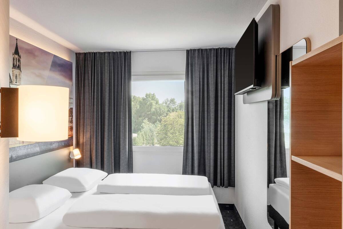 Een hotelkamer met een bed, een televisie, een raam met gordijnen en een lamp.