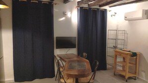 A room with a wooden dining table, two chairs, a TV, and a metal shelf unit.