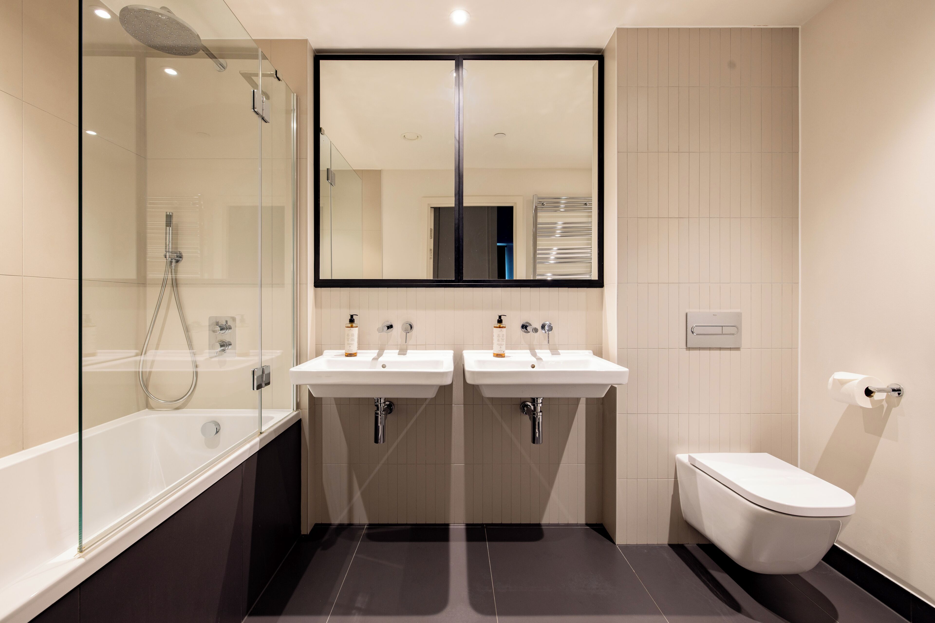 A modern bathroom with a glass-enclosed shower, two sinks, and a toilet.