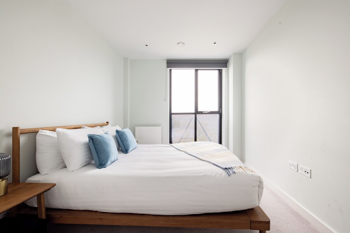 A bedroom with a large bed, a wooden headboard, a bedside table, and a window with a view.