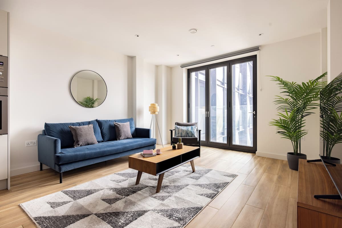 A modern living room with a blue sofa, a wooden coffee table, and a large mirror on the wall.