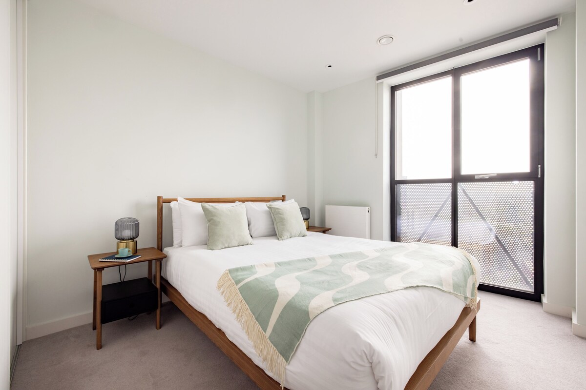 A bedroom with a bed, bedside table, lamp, and a large window with a view.