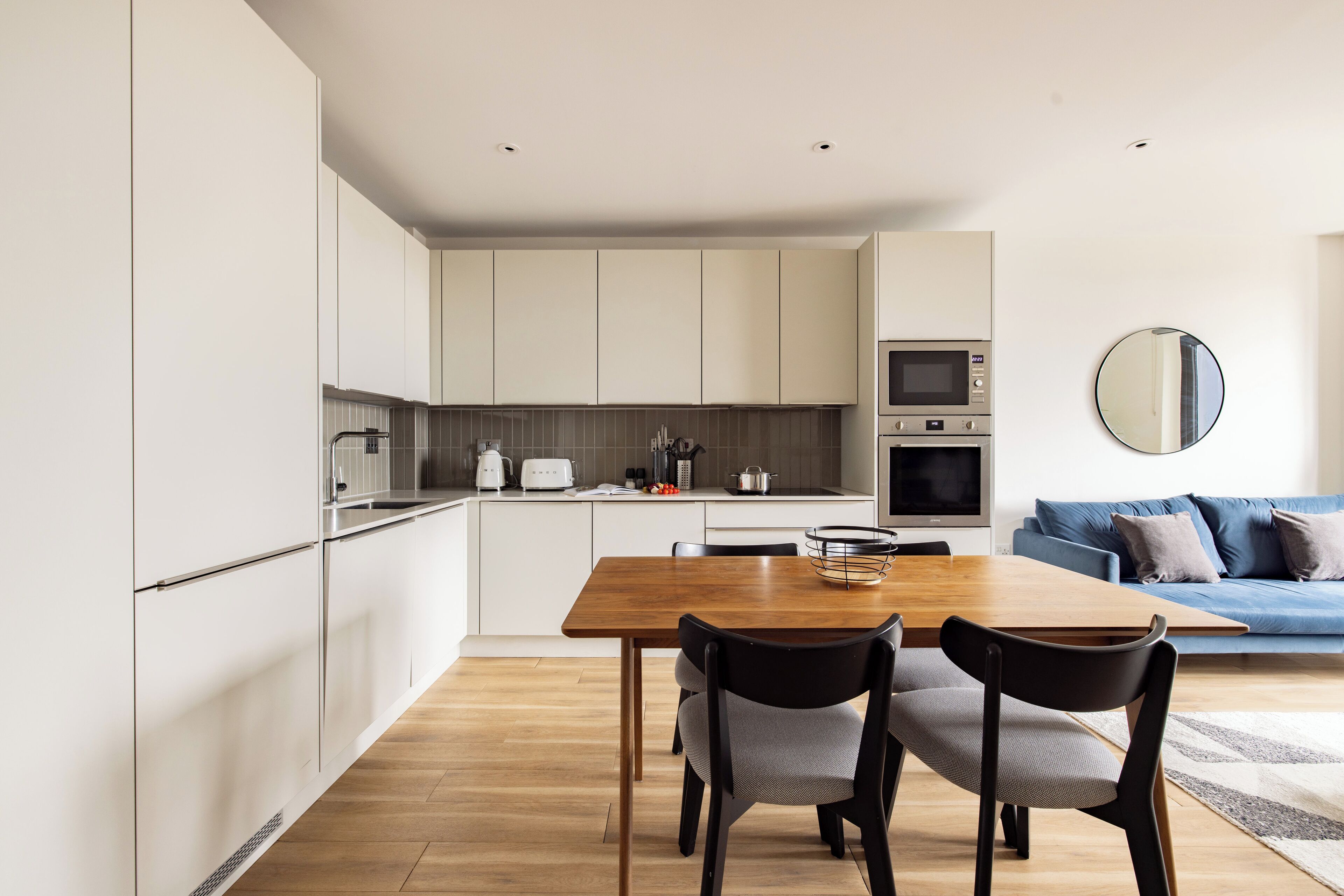 Una cocina moderna con armarios blancos, una mesa de comedor de madera y un sofá azul en la sala de estar.