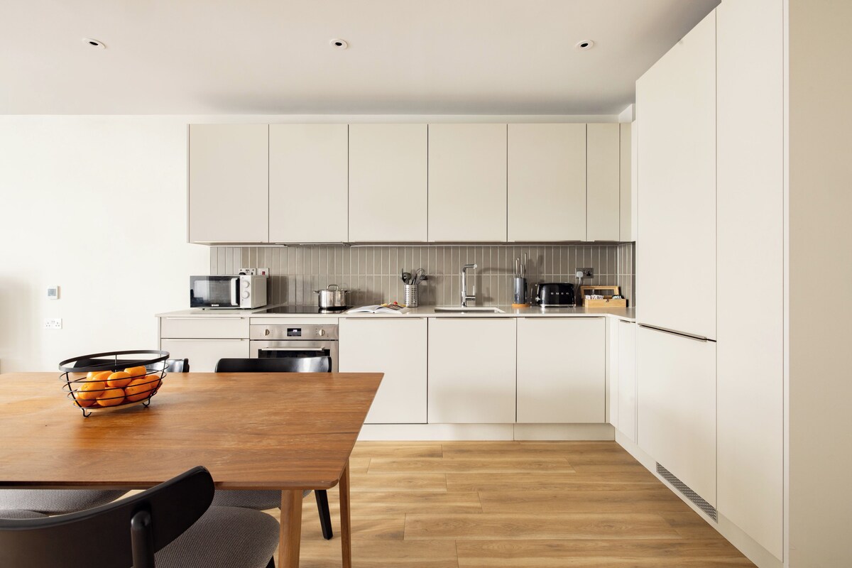 A modern kitchen with white cabinets, a wooden dining table, and a black chair.