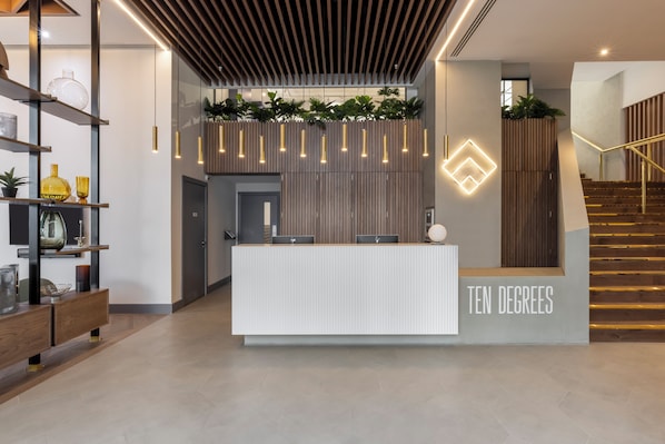 A reception desk with a sign reading "TEN DEGREES" and a staircase with wooden railings. - Croydon by Charles Hope (Croydon)
